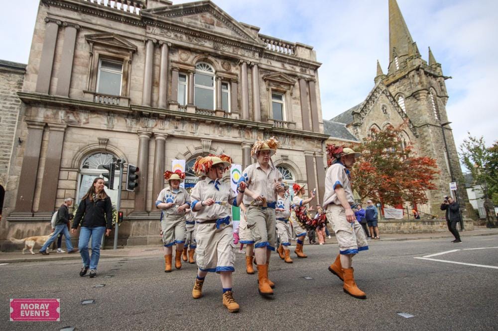 Victorian street parade in Moray, featuring participants in period costumes and hats during a local event. Historic architecture and autumn trees enhance the festive atmosphere in Moray, Scotland.