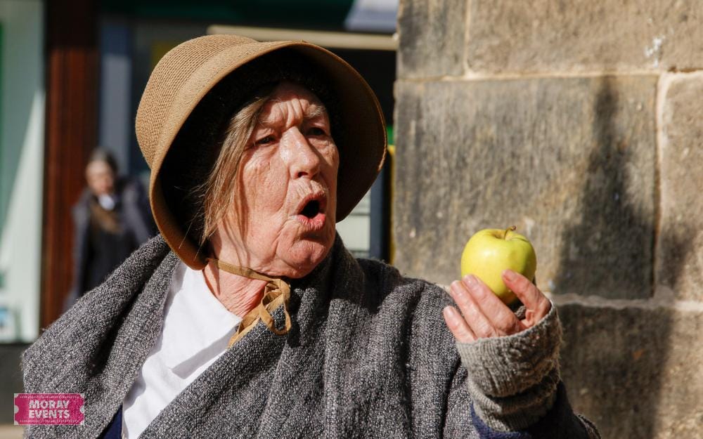 Woman dressed in vintage costume holding a green apple at Moray Events, Scottish heritage festival, outdoor event, historical reenactment, entertainment in Moray region, popular local celebration.