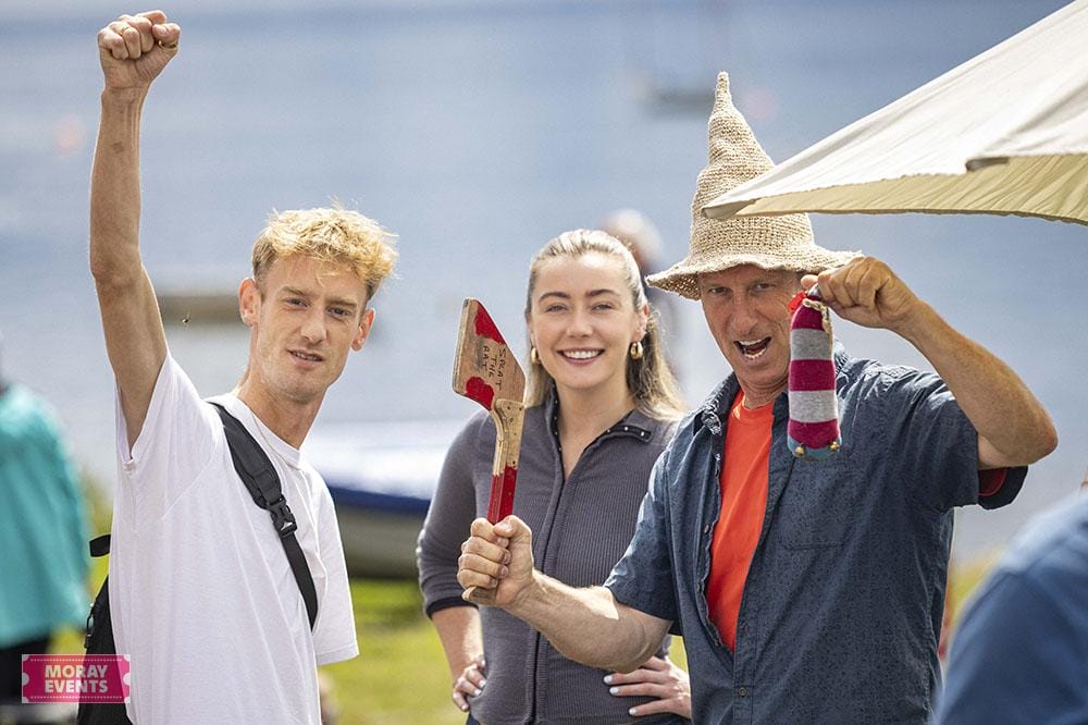 Young man celebrating at Moray Events by the water with family, under an umbrella, enjoying outdoor festivals, with festive accessories and a joyful atmosphere.