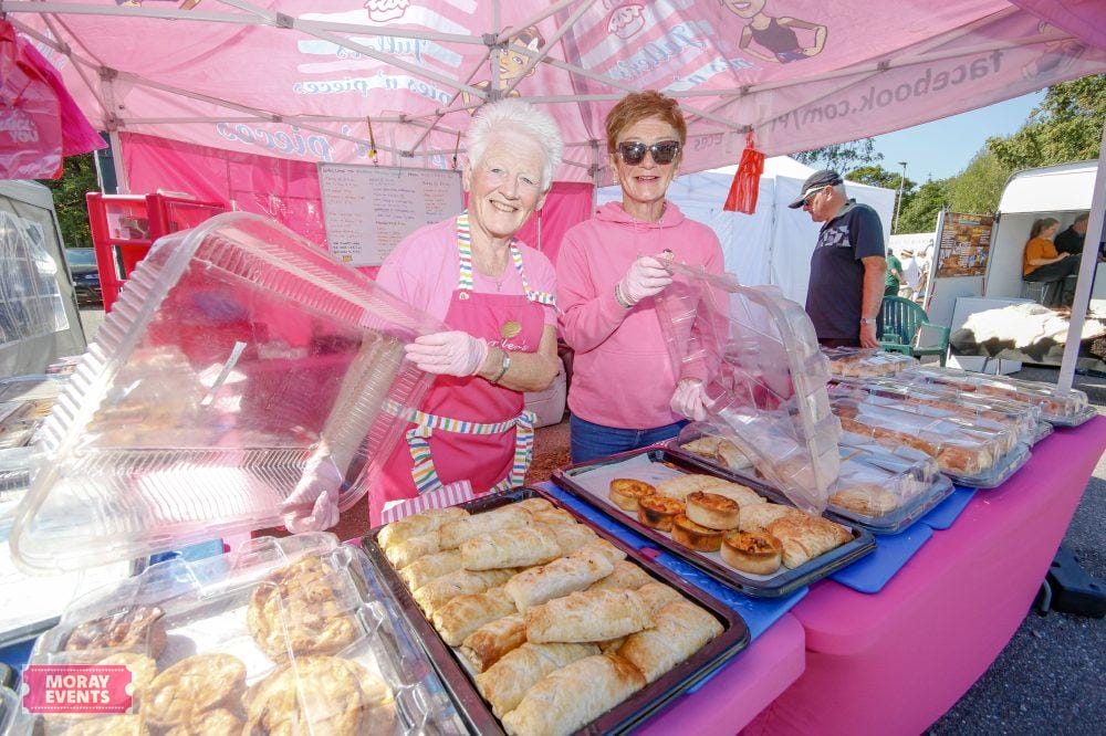 Delicious baked goods served at Moray Events outdoor market stall in Scotland, with cheerful vendors in pink aprons, showcasing pastries and cakes under a pink canopy for a vibrant local food event.