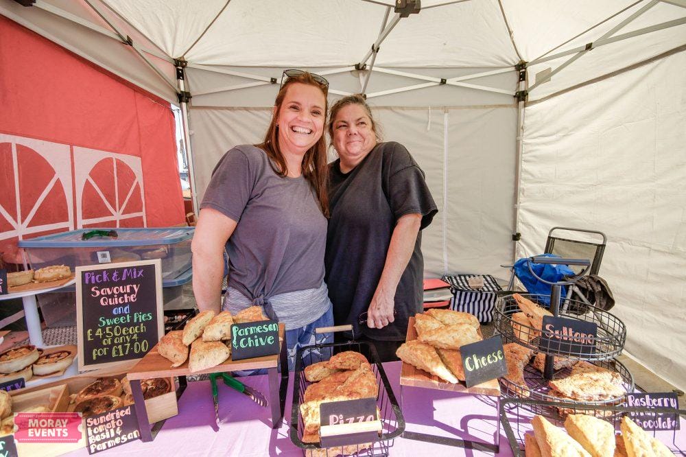 Vibrant outdoor food stall at Moray Events showcasing homemade quiches, sweet pies, and savoury treats with smiling vendors under a white tent, highlighting local event and craft food market atmosphere.