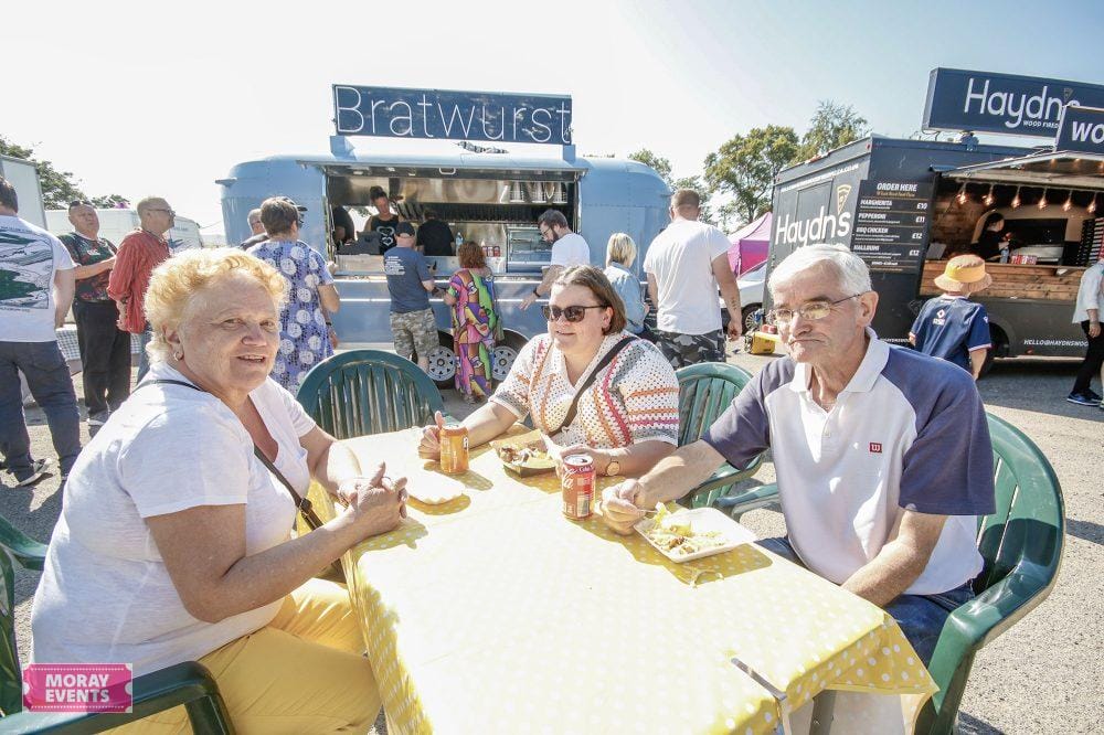 Vibrant outdoor food festival at Moray Events with people enjoying meals at a sunny table, featuring food trucks and community atmosphere in Moray, Scotland.
