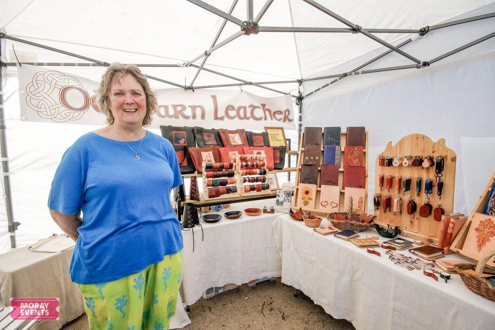 Handmade leather products display at Moray Events artisan market, featuring colourful wallets, belts, and accessories in a festive outdoor setting.