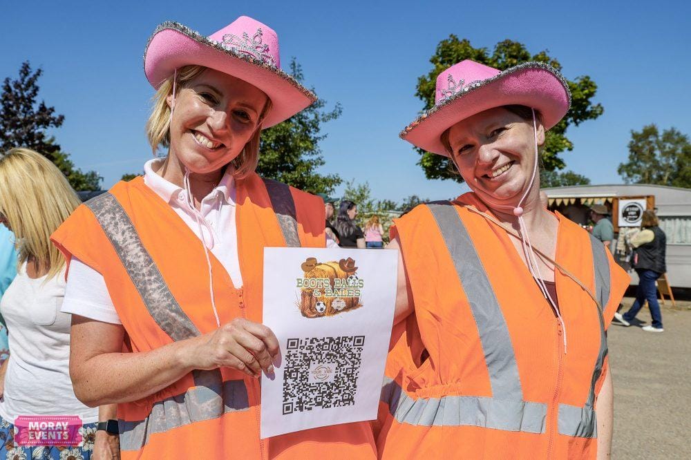 Brightly dressed women wearing pink cowboy hats and orange safety vests at Moray Events outdoor festival in Moray, Scotland, promoting community engagement and local activities.