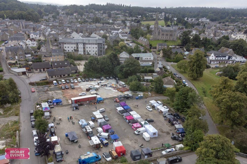 Vibrant outdoor market with colourful stalls and parked vehicles in Moray, Scotland, surrounded by lush greenery and historic buildings, ideal for local events and community gatherings.